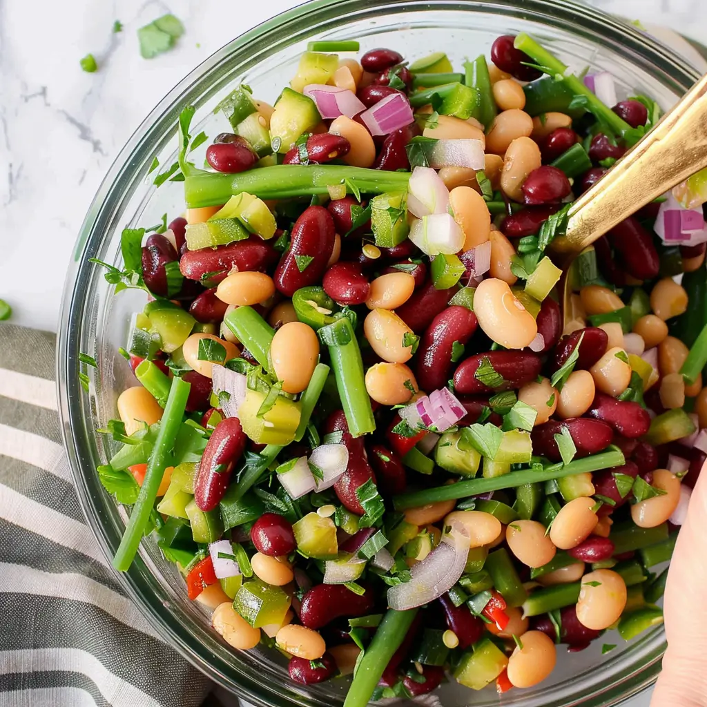 Overhead shot of kidney beans, chickpeas, green beans, celery, and red onion in bowls on white marble