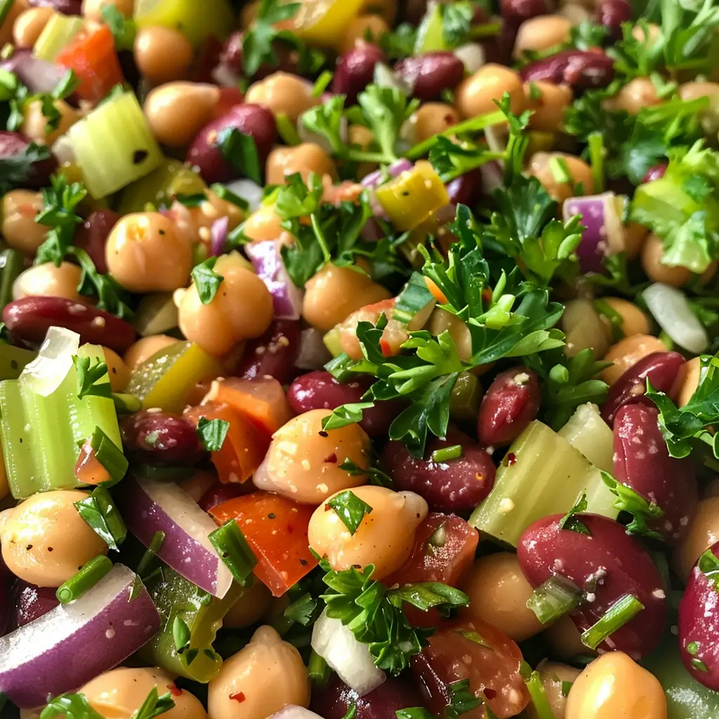 Overhead shot of three bean salad ingredients being tossed in a glass bowl on white marble